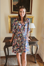 Gayle Belted Collard Mini Dress in Navy Floral with puff sleeves and V-neck, styled indoors with vintage decor. Elegant floral dress by Hermoza.