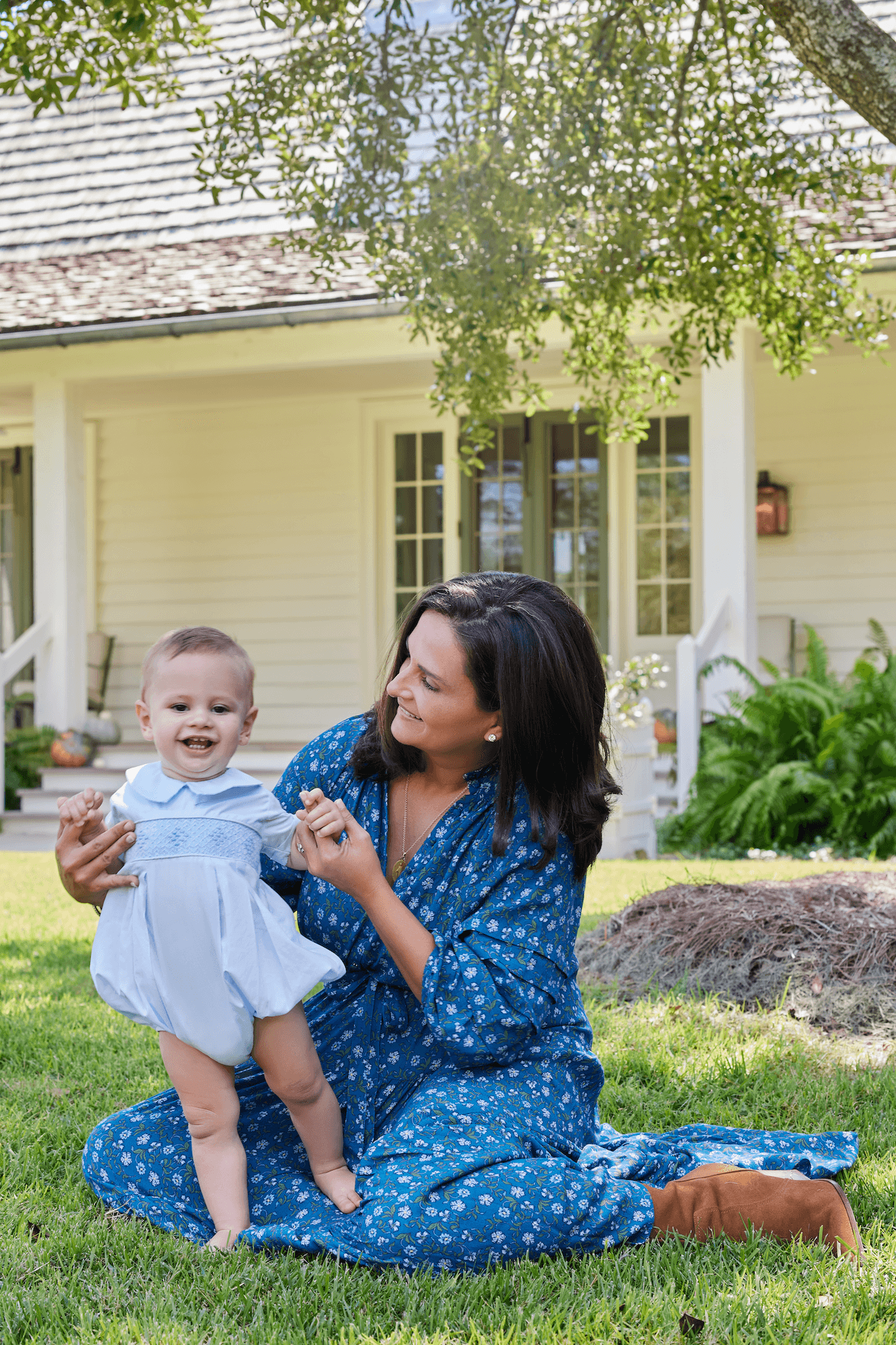 Woman wearing Zoey Jo Belted Tiered Maxi Dress in a garden setting, seated on grass while holding a smiling baby.