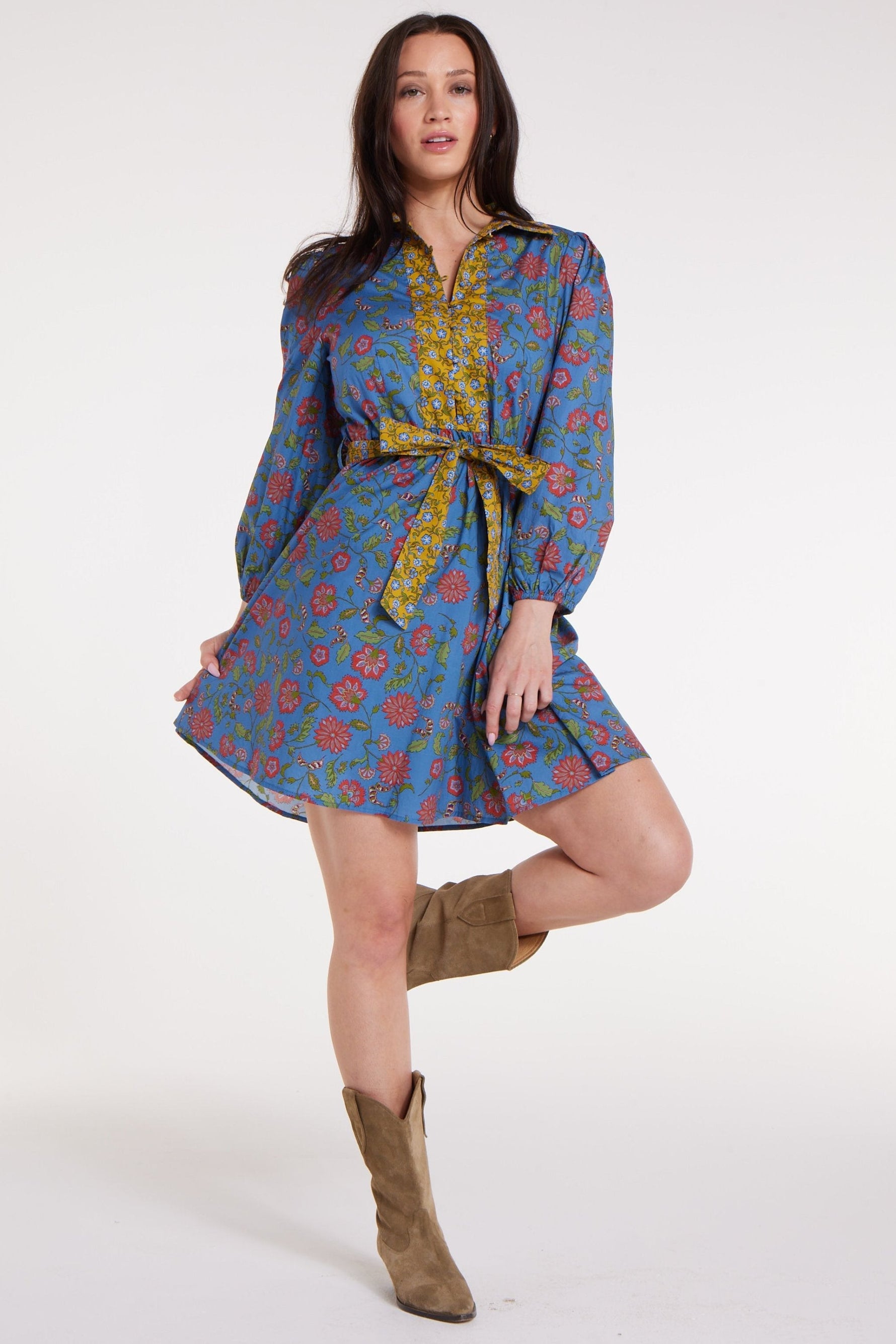 Model wearing Halle Collared Belted Mini Dress in Blue Floral with flared hem and yellow sash, styled with tan boots.